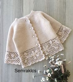 two crocheted sweaters sitting on top of a wooden table next to flowers