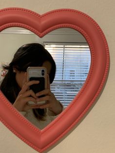 a woman taking a selfie in front of a heart shaped mirror