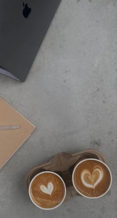 two cups of coffee with hearts on them next to an apple laptop and mouse pad