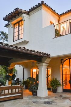 a large white house with lots of windows and plants on the front porch, next to a wooden bench