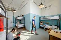 two men sitting on the floor in a dorm room with bunk beds and desks