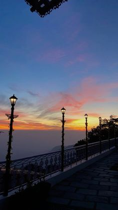 the sun is setting behind some street lamps and lights in front of a balcony with wrought iron railings