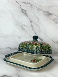 a white and green dish with a lid sitting on a marble counter top next to a ceramic platter