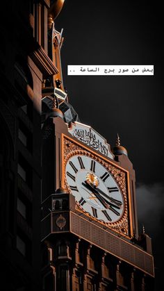 a large clock on the side of a building at night with an emblem in the background