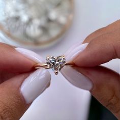 a woman's hand holding a ring with a heart shaped diamond on top of it