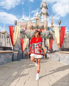 a woman in a red sweater and white skirt is walking down the street near a castle