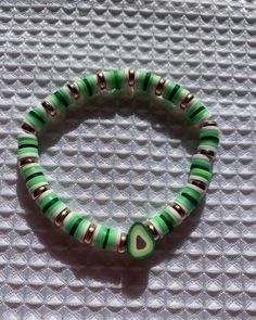 a green and gold beaded bracelet on a white surface with a heart charm in the middle