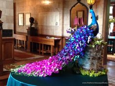 the peacock is sitting on the table with purple flowers in it's feathers and tail