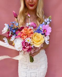 a woman holding a bouquet of flowers in front of a pink background with her hands behind her back