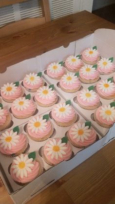 a box filled with pink and white cupcakes on top of a wooden table