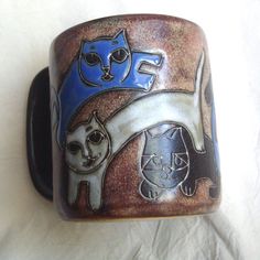 two cats are sitting on top of a brown and blue ceramic cufflinker that is laying on a white sheet