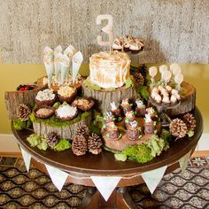 a table topped with cakes and cupcakes on top of wooden slices covered in moss