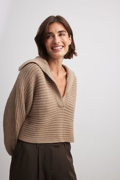 This sweater is knitted and features a v-neck design with a collar, dropped shoulders, wide long sleeves with ribbed cuffs at the hems, a chunky rib design and a cropped, oversized fit. Oversized V-neck Polo Sweater For Fall, Trendy Knit Polo Sweater With Ribbed Cuffs, Oversized Knit Cropped Sweater With Ribbed Collar, Oversized Cozy Cropped Sweater With Ribbed Collar, Cozy Oversized Cropped Sweater With Ribbed Collar, Oversized Knit Polo Sweater With Ribbed Collar, Trendy Ribbed Knit Polo Sweater, Fall Ribbed Collar Knit V-neck Sweater, Oversized V-neck Cropped Knit Sweater