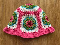 a crocheted pink and green hat sitting on top of a wooden table