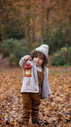 a little boy standing in leaves holding a lantern with one hand and looking at the camera