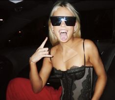 a woman with her tongue out and sunglasses on, sitting in the back seat of a car