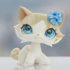 a small toy cat with blue eyes and a flower in its hair sitting on a table