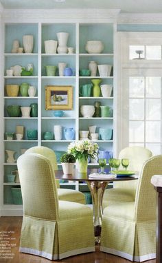 two yellow chairs sitting at a small table in front of a bookcase filled with dishes