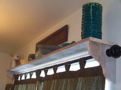 a kitchen window with curtains hanging from it's side and a green vase sitting on the ledge