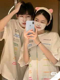 two people standing in front of a mirror taking a selfie with their cell phones