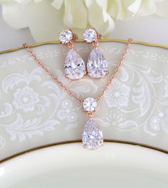 "Chic and elegant ! This set is created with rose gold finish and Swarovski Pure Brilliance stones. A perfect selection for your bridal party or a simple set for your wedding day. Available in 2 finishes. Necklace measures 15 inches and extends to 17 inches Pendant is 7/8\" long Earrings measure 7/8\"" Rose Gold Cubic Zirconia Drop Jewelry, Rose Gold Dangle Jewelry Sets With Matching Earrings, Rose Gold Dangle Necklaces With Matching Earrings, Gold Bridal Necklace Set, Dainty Rose Gold Necklace, Wedding Earrings Chandelier, Rose Gold Drop Earrings, Gold Bridal Necklace, Dainty Rose