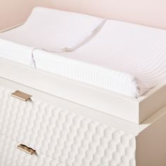 a white dresser with two drawers and a mattress on it's side, next to a pink wall