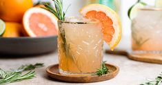 a drink with rosemary garnish on the rim next to sliced grapefruit