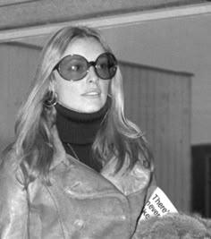 black and white photograph of woman in leather jacket with sunglasses on her face, looking off to the side