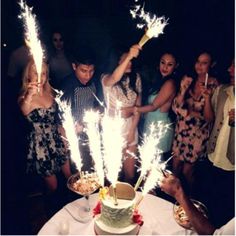 a group of people standing around a cake with sparklers