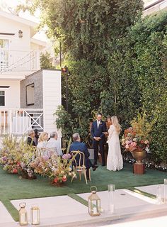 a bride and groom are getting married in front of a house with flowers on the lawn