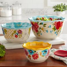 three flowered bowls are sitting on a kitchen counter with utensils and napkins