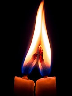 two lit candles in the dark with one burning