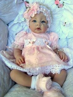 a baby doll wearing a pink dress and bonnet sitting on a white blanket with flowers