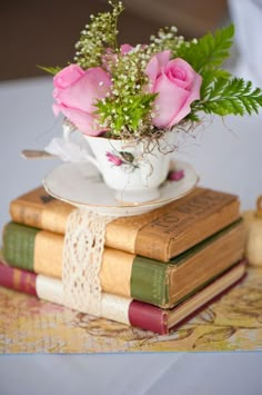 pink roses are in a teacup on top of three books, sitting on a table