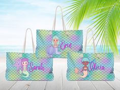 three bags with mermaids on them sitting on a wooden table next to the ocean