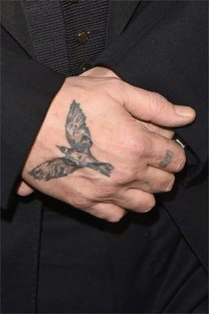 a man with a bird tattoo on his left arm and wrist, wearing a black suit