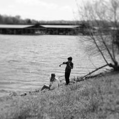 black and white photograph of two people on the shore of a lake, one pointing at something