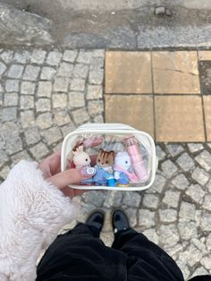 a person holding a small plastic container filled with stuffed animals on cobblestone pavement