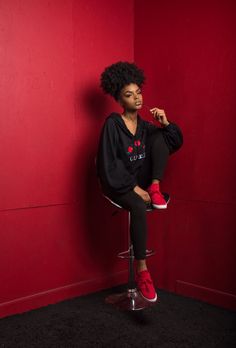 a woman sitting on top of a stool next to a red wall