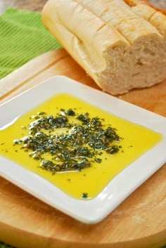 a white plate topped with bread next to a bowl of yellow liquid and sliced loaf of bread