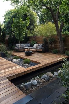 an outdoor living area with wooden decking and stone seating on the ground, surrounded by trees