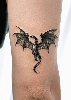 a black dragon tattoo on the side of a woman's leg, showing it's wings