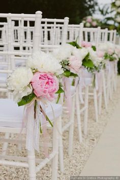 rows of white chairs with pink and white flowers tied to the back, along side each other