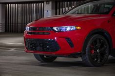 the front end of a red car parked in a parking lot with its lights on