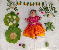 a baby is laying on the ground surrounded by flowers and leaves