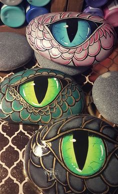 three painted rocks with green eyes on them