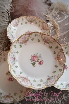 an assortment of antique china plates and saucers with pink roses on them, sitting on a lace tablecloth