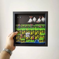 a hand holding up a framed video game artwork piece with an image of mario and luigi on it