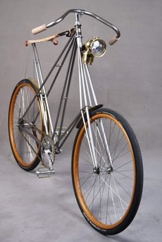 a silver and orange bike with wooden spokes on the front wheel, standing against a gray background