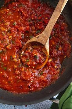 a wooden spoon in a pot filled with tomato sauce